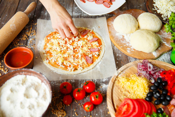 Cook in the kitchen putting the ingredients on the pizza. Pizza concept. Production and delivery of food - Photo, image