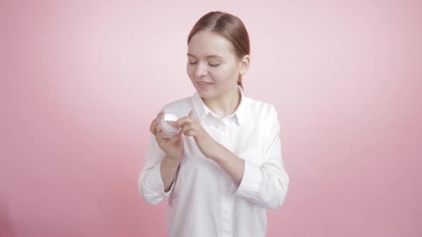 Beautiful girl with natural beauty puts white cream on her face and cheek. - Video