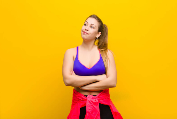 young blonde woman feeling happy, proud and hopeful, wondering or thinking, looking up to copy space with crossed arms. sport concept - Photo, image