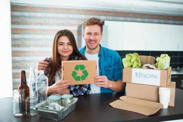 若い夫婦が台所でゴミを分別している。若い男と女が台所でリサイクル品を選別している。再生可能な段ボール、紙、鉄、プラスチック、ガラスなどの材料があります。. - 写真・画像