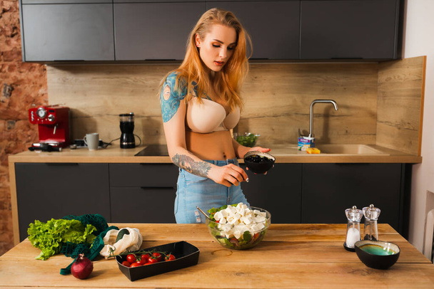 blond vrouw in lingerie voegt olijven naar kom met salade - Foto, afbeelding