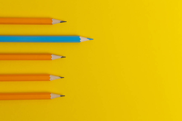 Blue pencil and orange pencils on a yellow paper background. Leader concept, different, unique. - Photo, image