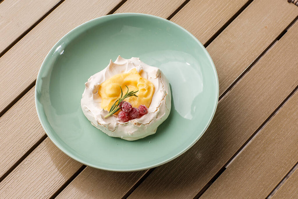 Pavlova mini cake with custard cream and fresh summer berries on green plate on wooden background. Baked meringue cake. - Фото, зображення