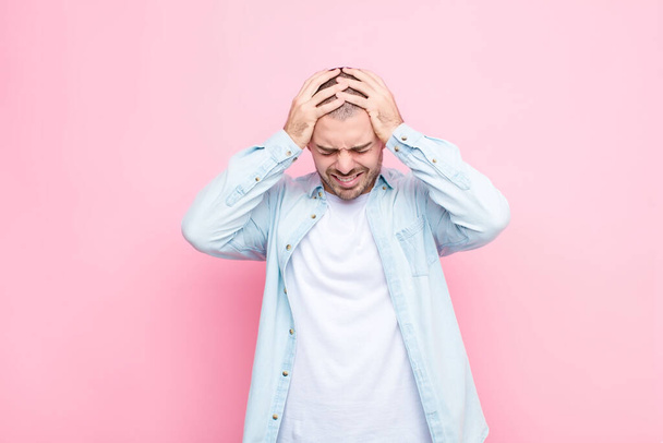 young handsome man feeling stressed and frustrated, raising hands to head, feeling tired, unhappy and with migraine against flat wall - Fotoğraf, Görsel