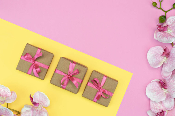 flatlay of Gift present boxes with pink ribbon, orchid flowers on pink yellow background. spring concept. Copy space - Photo, Image
