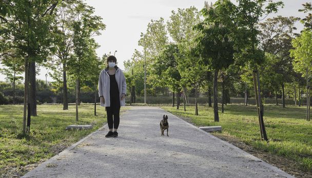 Single woman walking her dog in a park, keeping her social distance in a state of alarm because of the coronavirus. Coronavirus devices. Social distancing. Protection against pandemics - Photo, Image