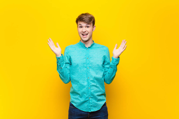young blonde man feeling happy, excited, surprised or shocked, smiling and astonished at something unbelievable isolated against flat wall - Photo, image