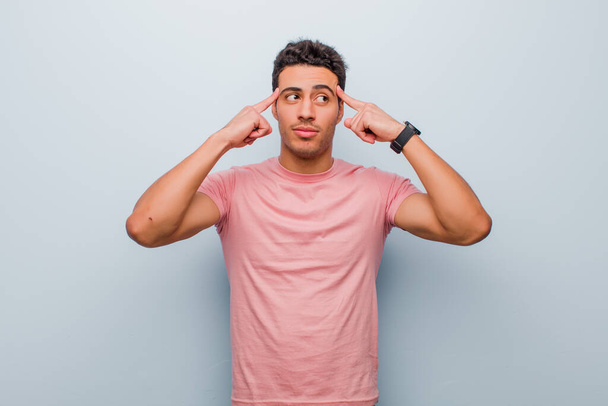 young arabian man feeling confused or doubting, concentrating on an idea, thinking hard, looking to copy space on side against gray wall - Fotoğraf, Görsel