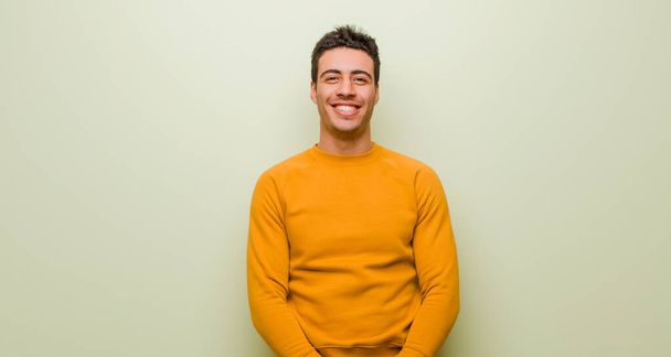 young arabian man looking happy and goofy with a broad, fun, loony smile and eyes wide open against flat wall - 写真・画像