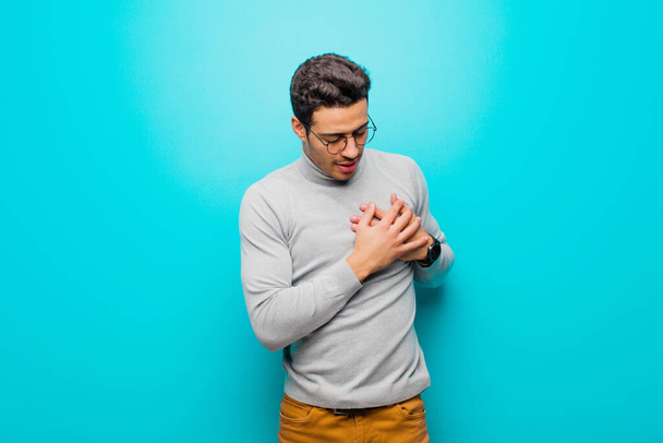 young arabian man looking sad, hurt and heartbroken, holding both hands close to heart, crying and feeling depressed against flat wall - Foto, Bild