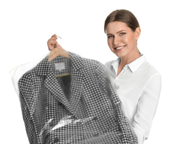 Young woman holding hanger with jacket in plastic bag on white background. Dry-cleaning service - Photo, image