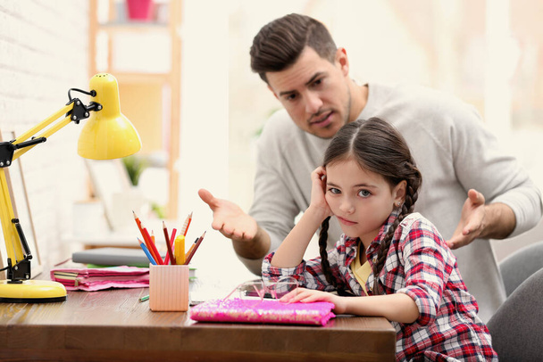 Father scolding his daughter while helping with homework at table indoors - Photo, Image