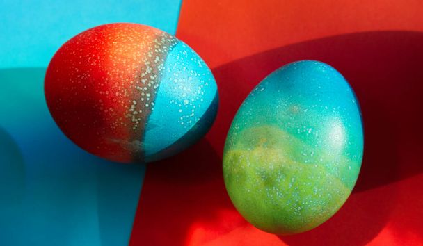 Vivid colored eggs for Easter standing on red and blue papers background - Photo, Image