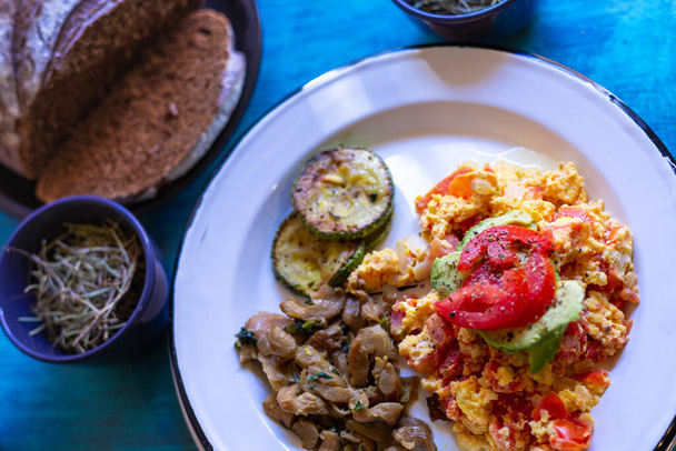 Mexican eggs with bread, mushrooms and zucchini, on white plate on blue table - Photo, Image