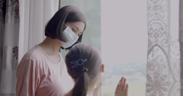 Matka z córką dziecko w masce patrząc przez okno - Materiał filmowy, wideo
