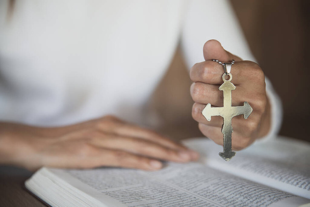 Ένα κορίτσι που κάθεται και μελετάει τις γραφές. Το άλλο χέρι κρατάει ένα σταυρό. Χριστιανικές εκπαιδευτικές έννοιες Η Αγία Γραφή ανοίγει και προσεύχεται στο Θεό. - Φωτογραφία, εικόνα