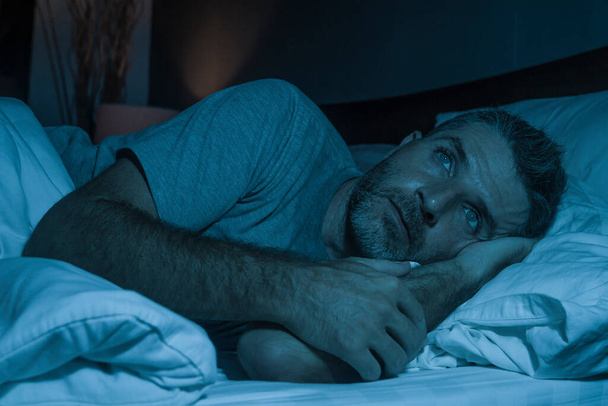 dramatic portrait in the dark of attractive depressed and worried man on bed suffering depression crisis and anxiety feeling lost lying sleepless in insomnia and life problem concept - Photo, image