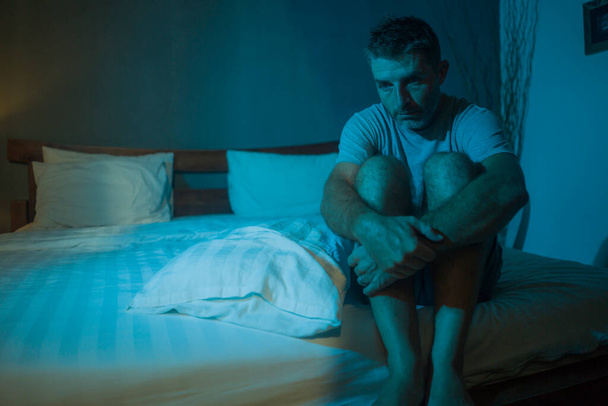 dramatic portrait in the dark of attractive depressed and worried man on bed suffering depression crisis and anxiety feeling lost sitting sleepless in insomnia and life problem concept - Foto, Bild