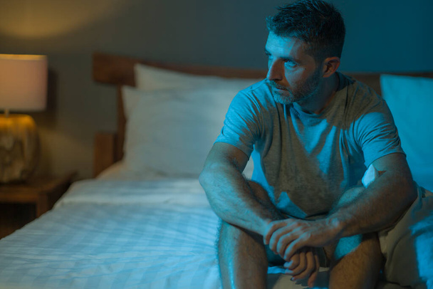 dramatic portrait in the dark of attractive depressed and worried man on bed suffering depression crisis and anxiety feeling lost sitting sleepless in insomnia and life problem concept - Photo, image