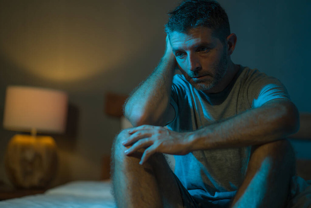dramatic portrait in the dark of attractive depressed and worried man on bed suffering depression crisis and anxiety feeling lost sitting sleepless in insomnia and life problem concept - 写真・画像