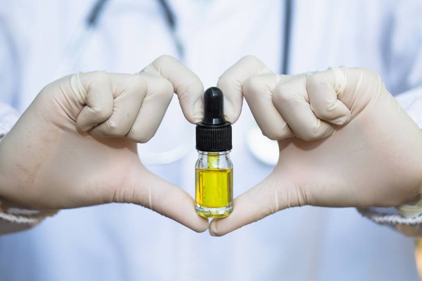 Doctors or researchers make heart-shaped symbols, holding a bottle of marijuana. CBD concept. Short-term marijuana oil. Alternative medicine. Extracts that are used to treat dangerous diseases. - Photo, image