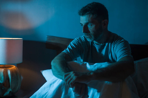 dramatic portrait in the dark of attractive depressed and worried man on bed suffering depression crisis and anxiety feeling lost sitting sleepless in insomnia and life problem concept - 写真・画像