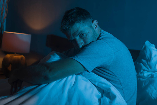 dramatic portrait in the dark of attractive depressed and worried man on bed suffering depression crisis and anxiety feeling lost sitting sleepless in insomnia and life problem concept - Fotoğraf, Görsel