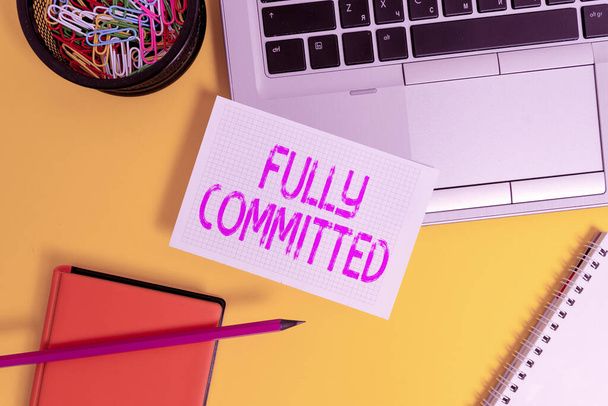 Text sign showing Fully Committed. Conceptual photo Extremely agreed to do something in life definitely Laptop pencil sheet clips container spiral notebook colored background. - Photo, Image