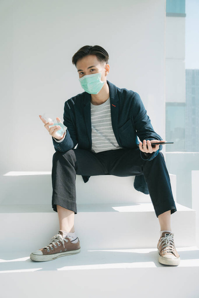 Retrato de moda - Jovem asiático tailandês homem quarentena-se em casa. Usando máscara de médico e segurando álcool gel
. - Foto, Imagem