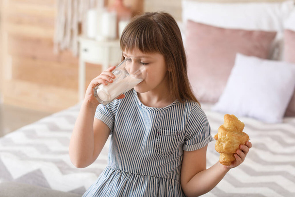 Little girl drinking milk with croissant in bedroom - Фото, изображение