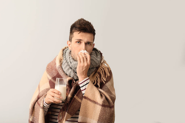 Joven enfermo con gripe sosteniendo vaso de leche sobre fondo gris
 - Foto, Imagen