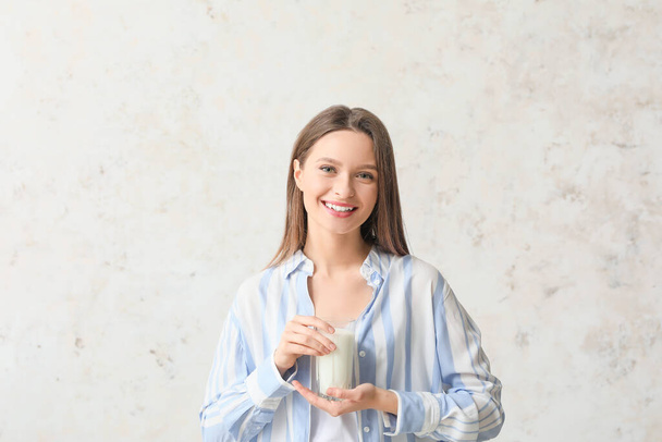 Jonge vrouw met glas melk op lichte achtergrond - Foto, afbeelding