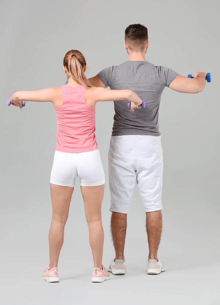 Sporty young couple training with dumbbells on grey background - Foto, imagen