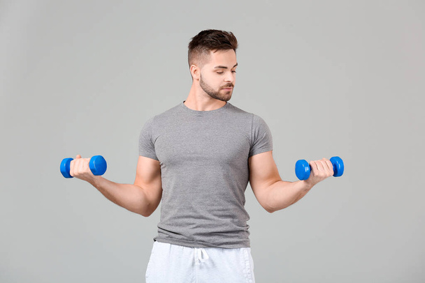 Sporty young man training with dumbbells on grey background - Fotografie, Obrázek
