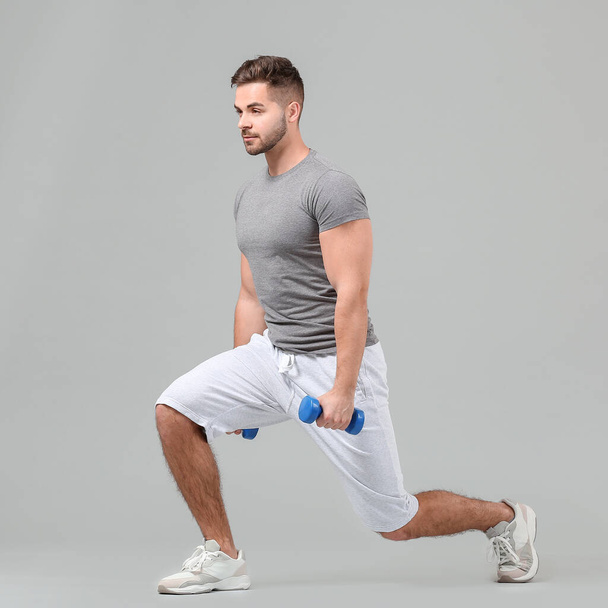 Sporty young man training with dumbbells on grey background - Photo, image