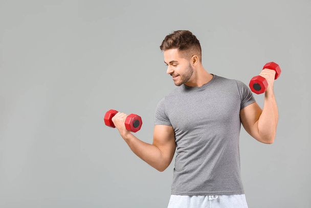 Sporty young man training with dumbbells on grey background - Photo, Image