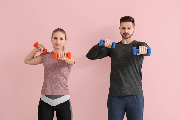 Sporty young couple training with dumbbells on color background - Foto, afbeelding
