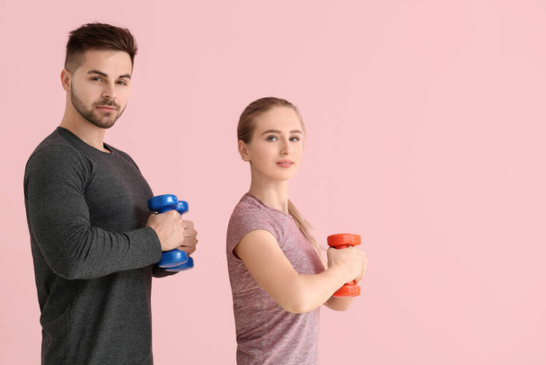 Sporty young couple training with dumbbells on color background - 写真・画像