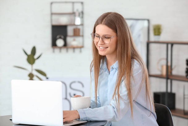Jonge vrouw drinken van koffie tijdens het werken op laptop in cafe - Foto, afbeelding