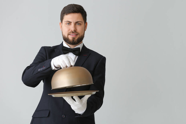 Handsome male waiter with tray and cloche on grey background - Photo, Image