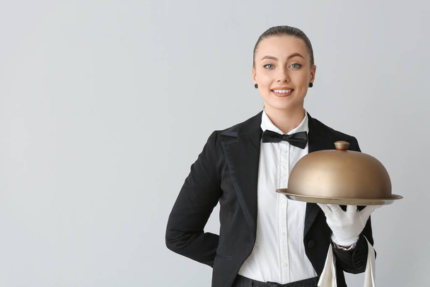 Γυναίκα σερβιτόρος με δίσκο και πανιά σε γκρι φόντο - Φωτογραφία, εικόνα