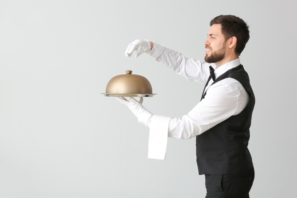 Αρσενικό σερβιτόρος με δίσκο και πανιά σε γκρι φόντο - Φωτογραφία, εικόνα