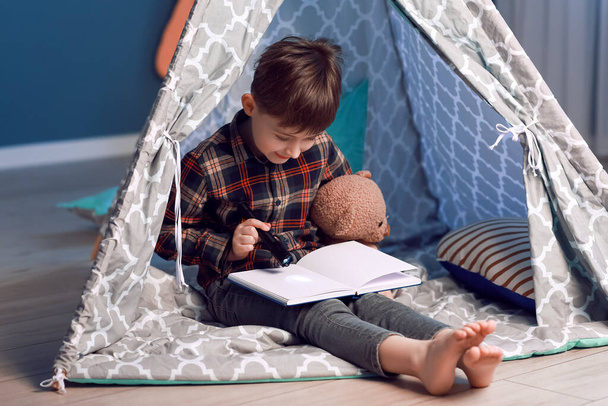 Küçük çocuk geceleri oyun çadırında kitap okuyor. - Fotoğraf, Görsel