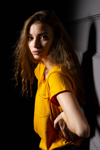 Young girl in a yellow T-shirt in a dark room - Фото, зображення