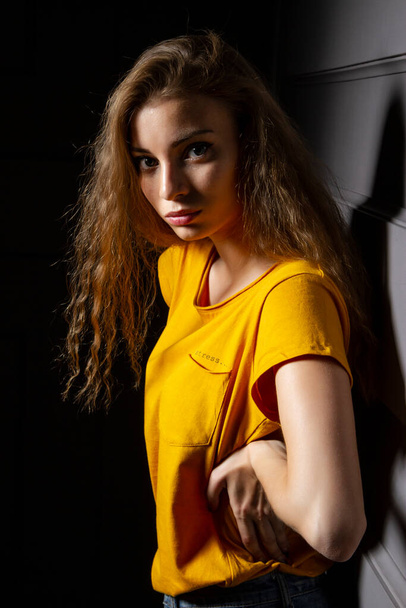 Νεαρή κοπέλα με κίτρινο μπλουζάκι σε σκοτεινό δωμάτιο - Φωτογραφία, εικόνα