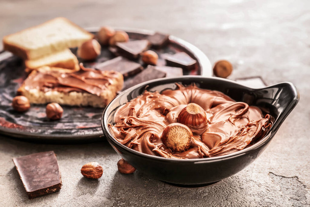 Bowl with tasty chocolate paste and hazelnuts on grunge background - Photo, Image