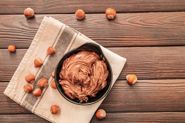 Bowl with tasty chocolate paste and hazelnuts on table - Valokuva, kuva