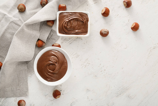 Ciotole con gustosa pasta di cioccolato e nocciole su sfondo chiaro - Foto, immagini