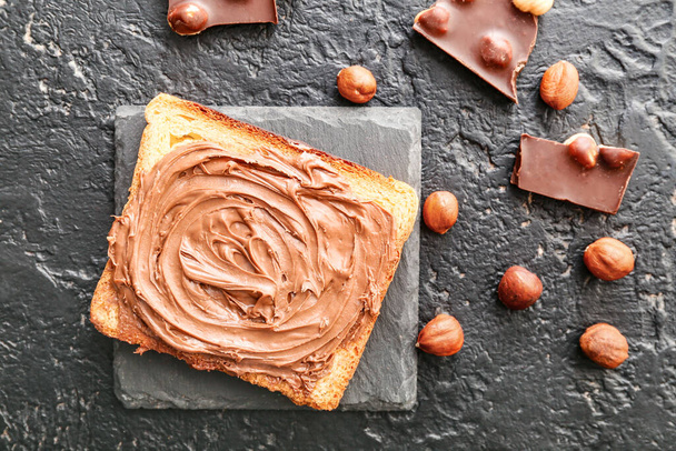 Fresh bread with chocolate paste and hazelnuts on dark background - Photo, Image