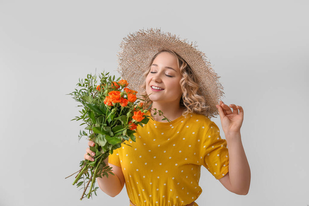 Όμορφη νεαρή γυναίκα με μπουκέτο λουλούδια στο φως φόντο - Φωτογραφία, εικόνα